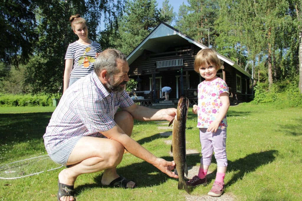 Kalastusretken tulos, kalasaaliina hauki. Pieni lapsi poseeraa kalan vieressä. Aholan mökit Padasjoki.